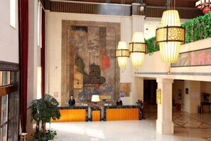 Eine Hotelhalle mit Rezeption, einer großen Wandmalerei, Pendelleuchten und einer Pflanze.