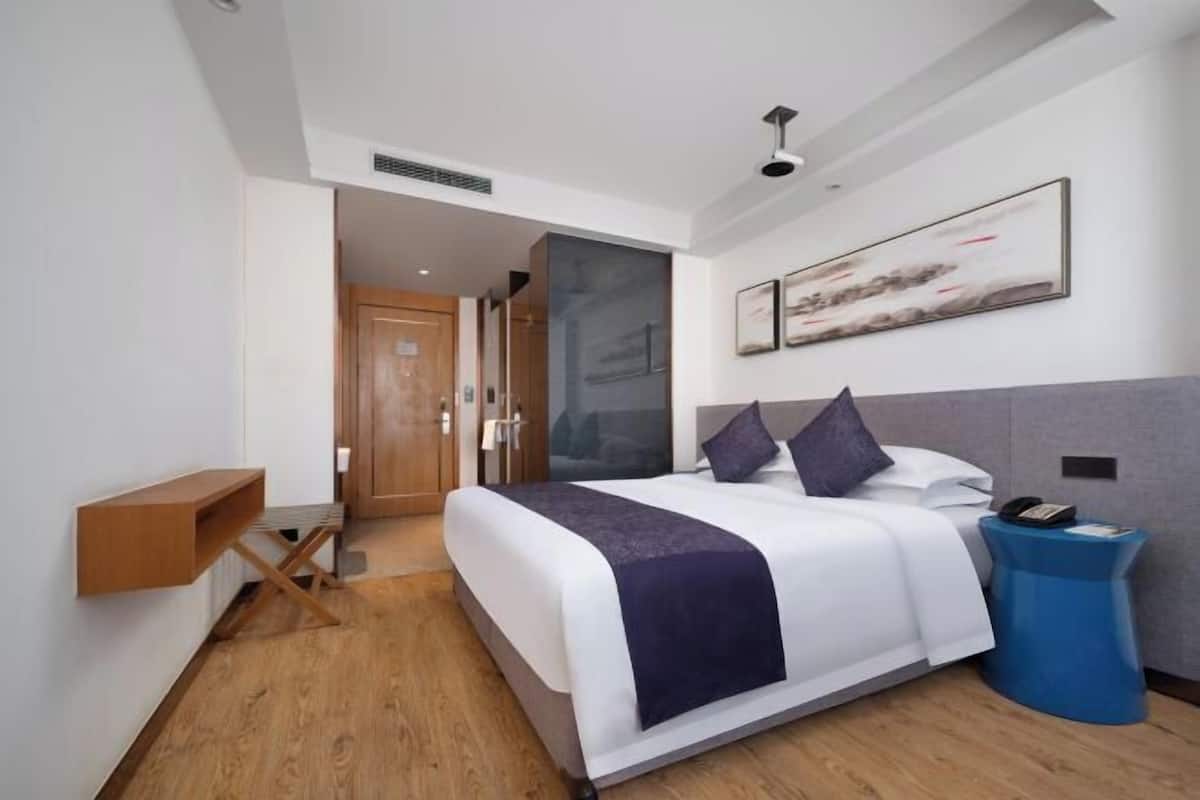 Una habitación de hotel moderna con una cama grande, una mesita de noche, una mesita auxiliar azul y un cuadro en la pared.