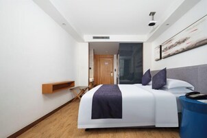 Una habitación de hotel moderna con una cama grande, un escritorio con silla, una obra de arte colgada en la pared y piso de madera.