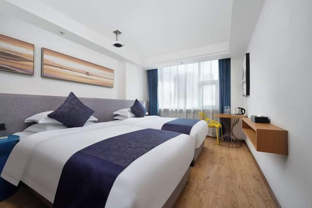 Habitación de hotel con dos camas, un escritorio, una silla, una mesita y una ventana con cortinas.