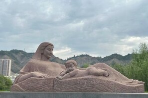 Una gran escultura al aire libre de una mujer y un niño reclinados, con colinas y un cielo nublado de fondo.