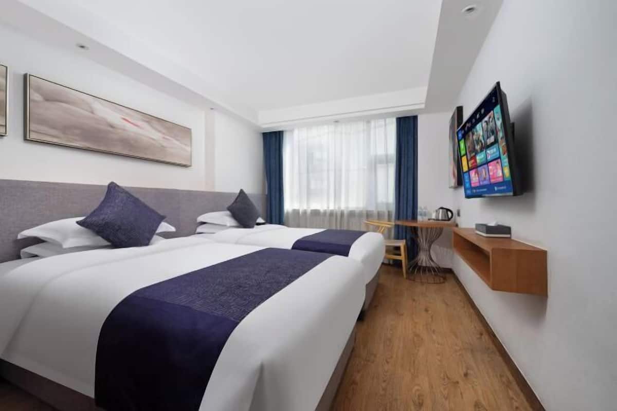 Habitación de hotel con dos camas, un escritorio, una silla, un televisor y una ventana con cortinas.