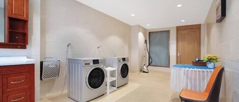 A laundry area with a washing machine, dryer, and a table with a chair.