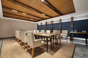 Un salón de conferencias con una larga mesa, sillas y un techo alto con vigas de madera.