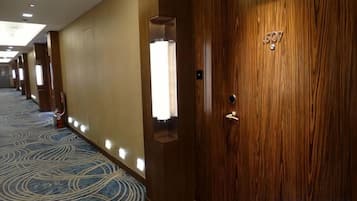 Corredor de hotel com portas de madeira, carpete estampado e iluminação embutida.