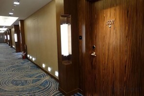 Un pasillo de hotel con puertas de madera, alfombra estampada e iluminación empotrada.