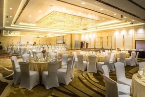 Un salón de banquetes con mesas redondas, sillas blancas y un escenario.