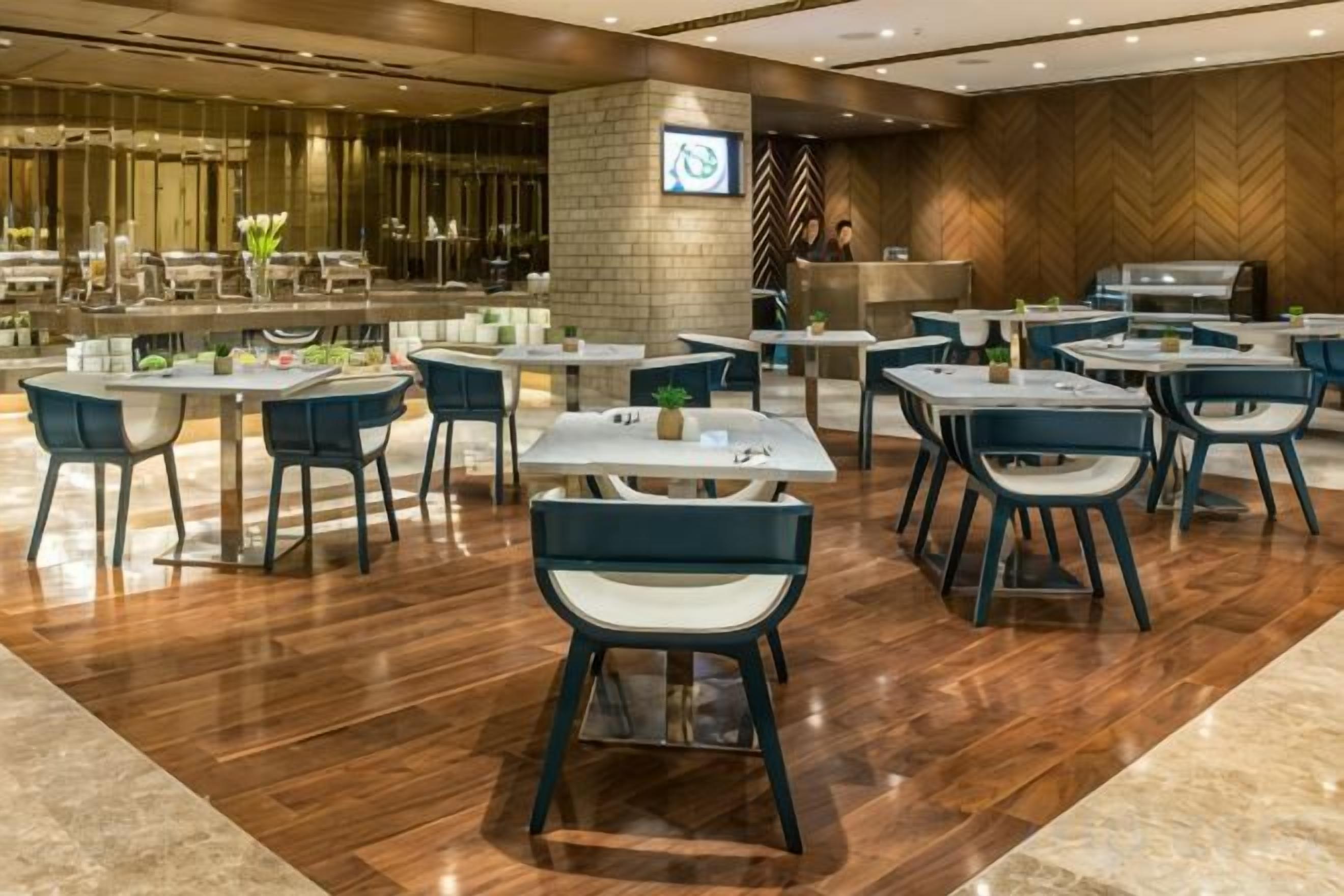A restaurant area with multiple tables and chairs, a counter with a coffee machine, and a herringbone-patterned wall.