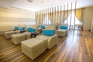 Un área de estar moderna con sofás y otomanas de cuero, suelo de madera y un ventanal con cortinas.