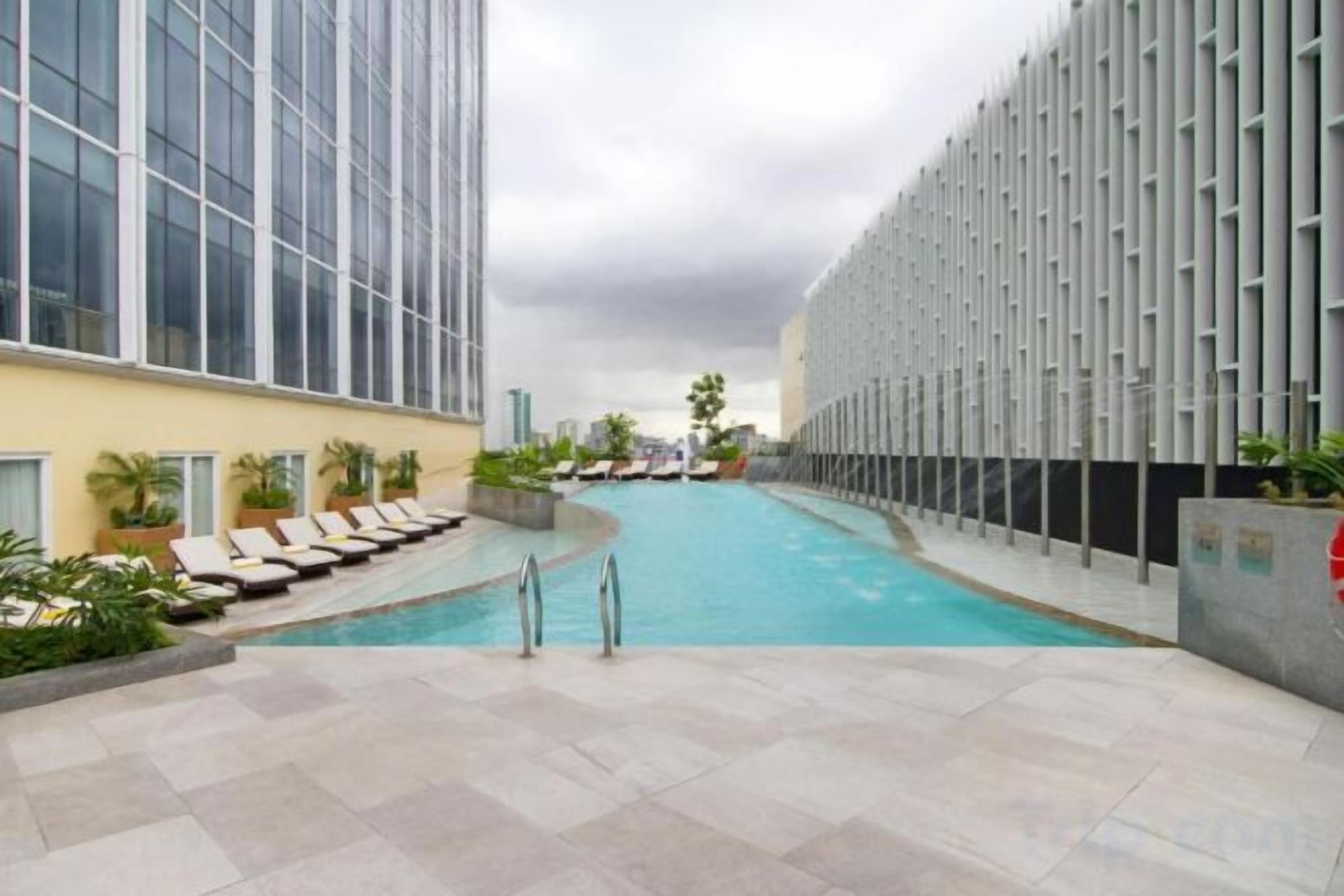 Área de piscina com espreguiçadeiras, piscina e um edifício moderno com fachada de vidro.