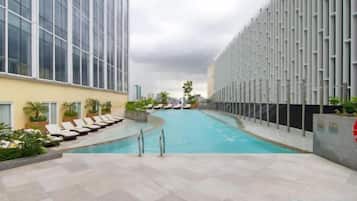 Et poolområde med liggestole, en pool og en moderne bygning med glasfacade.