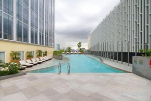Un área de piscina con sillones reclinables, una piscina y un edificio moderno con fachada de vidrio.