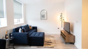 A modern living room with a dark blue sofa, a wooden TV stand, and a large mirror on the wall.