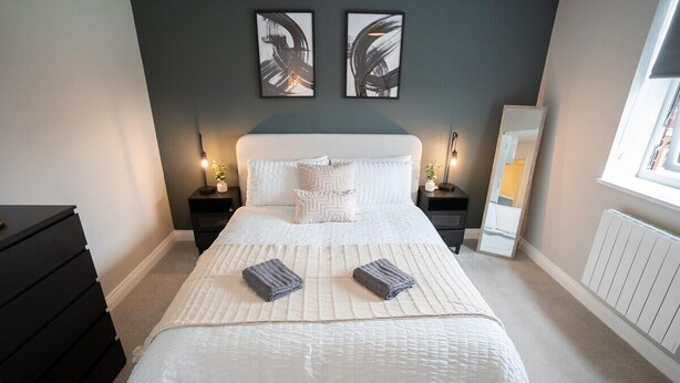 A neatly arranged bedroom with a large bed, two bedside tables, a dresser, and a window.