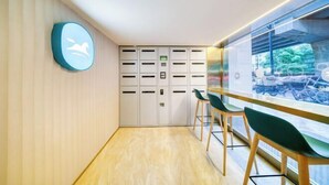 A modern waiting area with a row of lockers, a seating area with green chairs, and a view of parked bicycles through a glass wall. - HanTing Hotel (Hangzhou Wenyi Road) (Hangzhou)