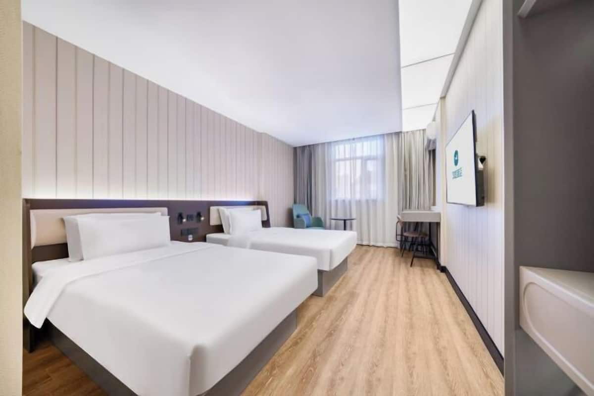 A hotel room with two beds, a desk, a chair, a TV, and a window with curtains.