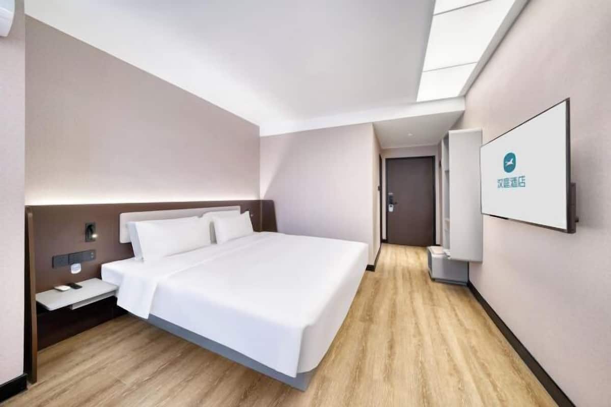 A modern hotel room with a large bed, bedside tables, a flat-screen TV, and a wooden floor.