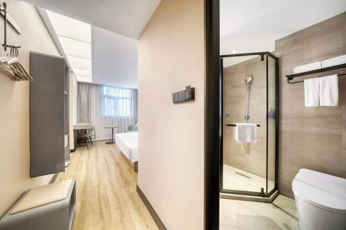 A hotel room with a wooden floor, a bed, a desk, and a shower area.