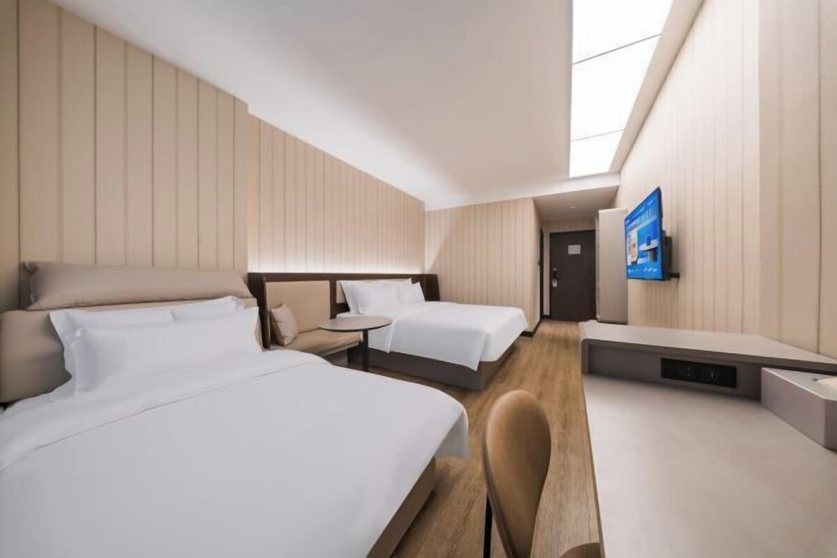 Une chambre d’hôtel avec deux lits, une petite table, une chaise et un téléviseur fixé au mur.