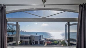 A modern room with a large panoramic window overlooking a beach and ocean.