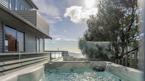A hot tub with a view of the ocean, a modern building with large windows, and a tree in the background.