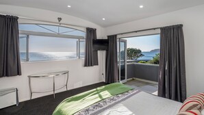 A hotel room with a bed, a small table, a TV, and a balcony with a view of the sea.