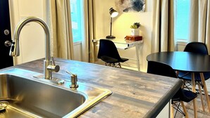Een moderne keuken met een roestvrijstalen spoelbak, een eethoek met tafel en stoelen, en een hanglamp.