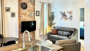 Een moderne keuken met een inbouwspoelbak, een eethoek met een tafel, en een woonkamer met een bank en een televisie.