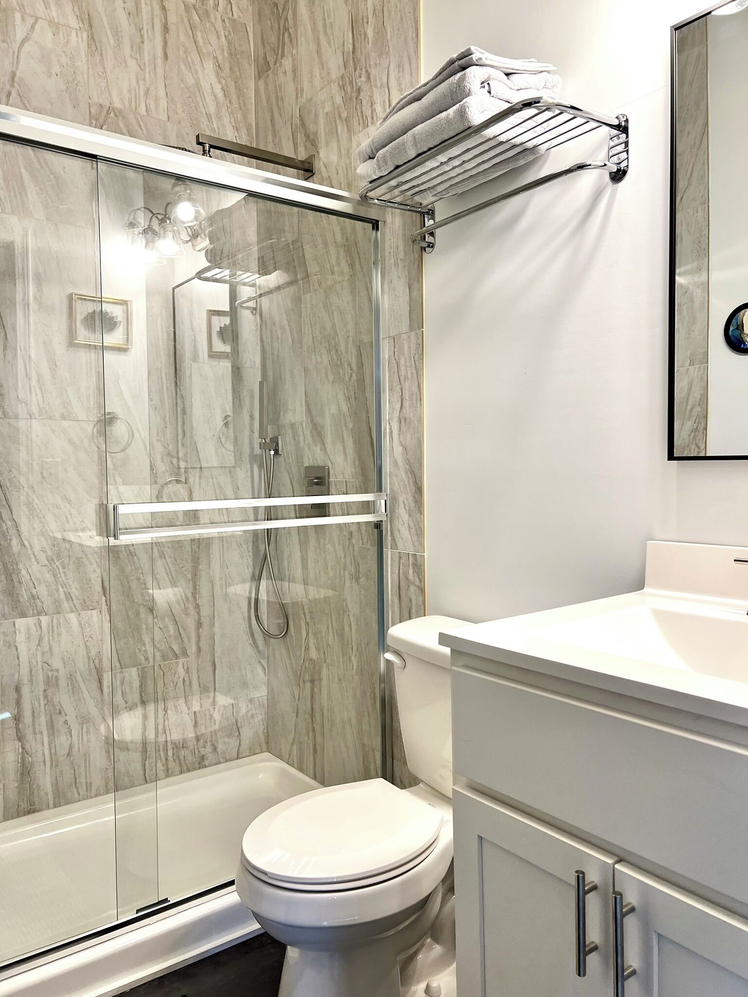 A modern bathroom with a glass-enclosed shower, a white toilet, and a vanity with a mirror.
