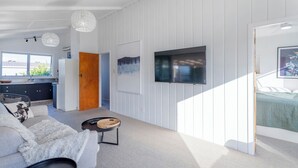 Una sala de estar moderna con un sofá, una mesa de centro, un televisor montado en la pared y una cocina al fondo.