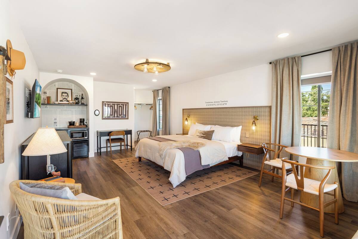 Ein modernes Hotelzimmer mit einem großen Bett, einem Essbereich, einer kleinen Küche und Blick ins Freie.