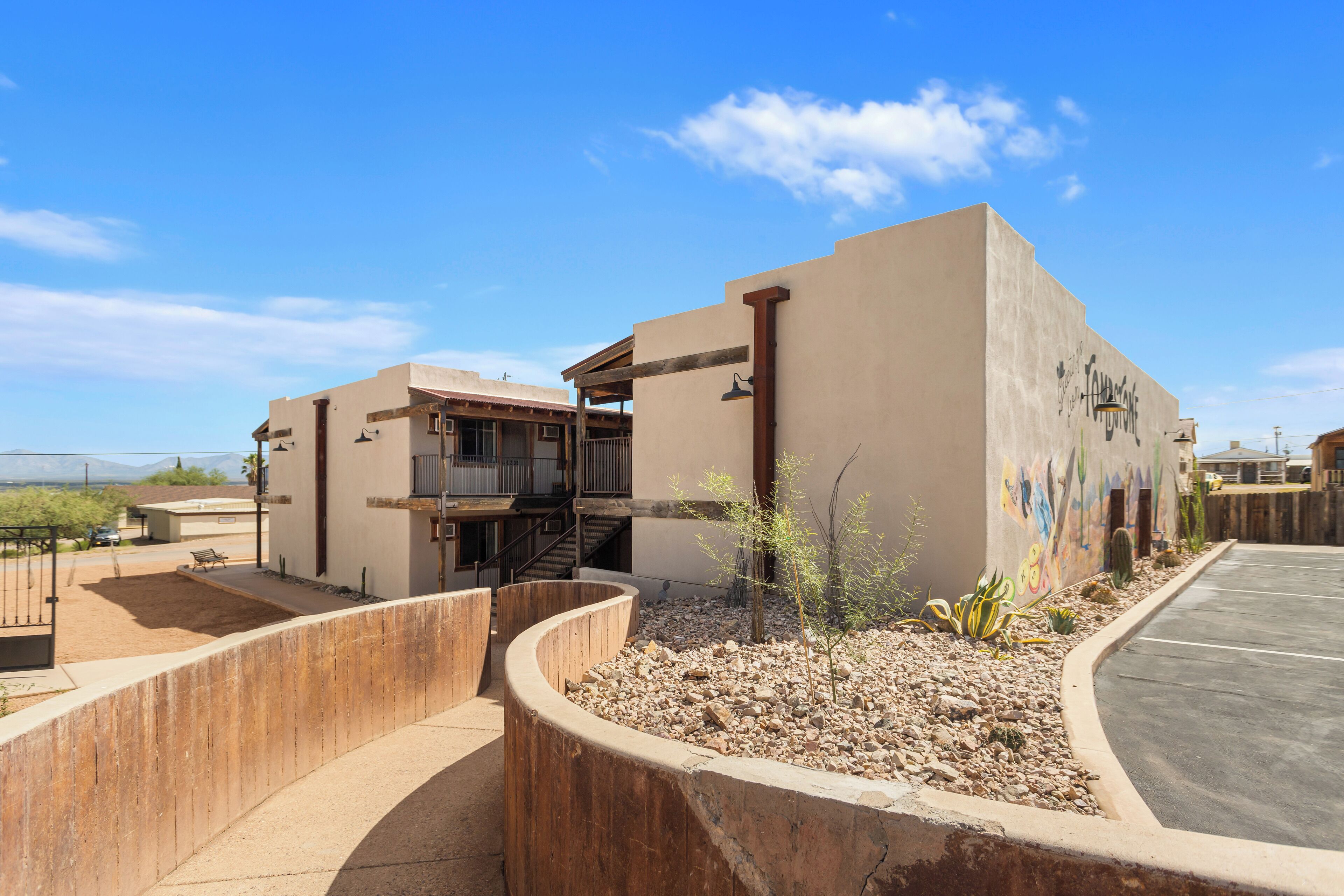A modern building with a curved concrete structure, a parking area, and a small garden with rocks and plants.