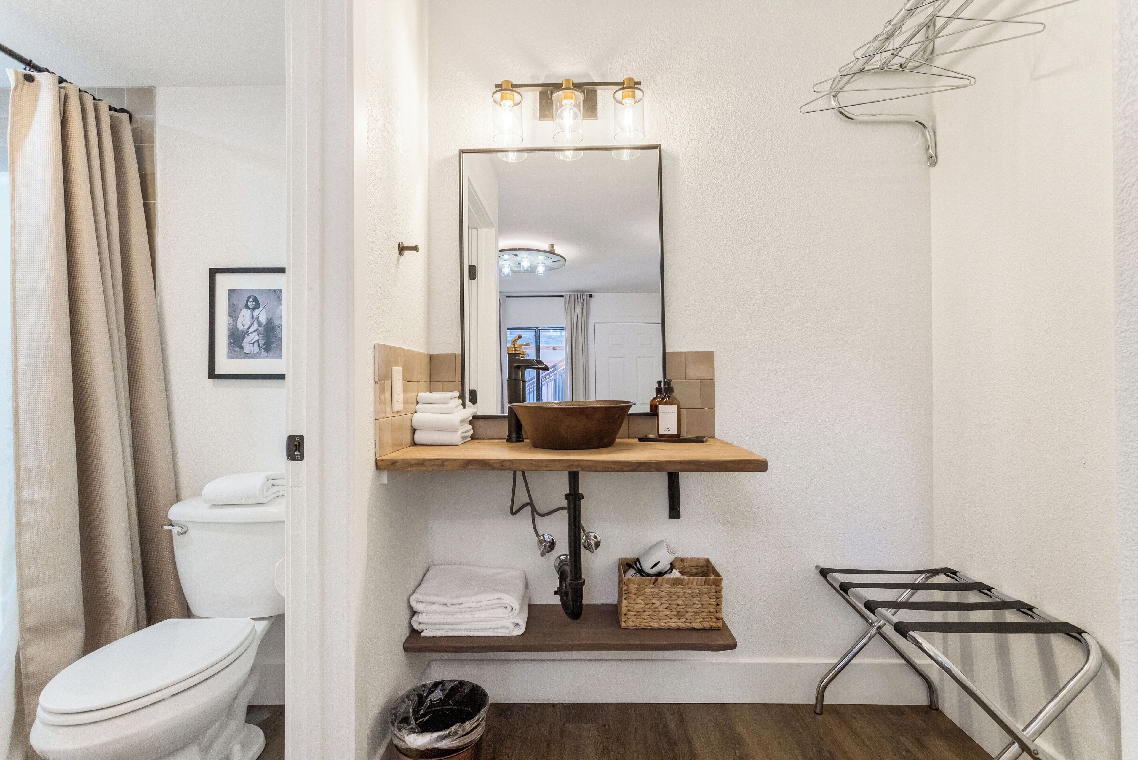 A bathroom with a toilet, sink with a mirror, towel rack, and a small trash bin.