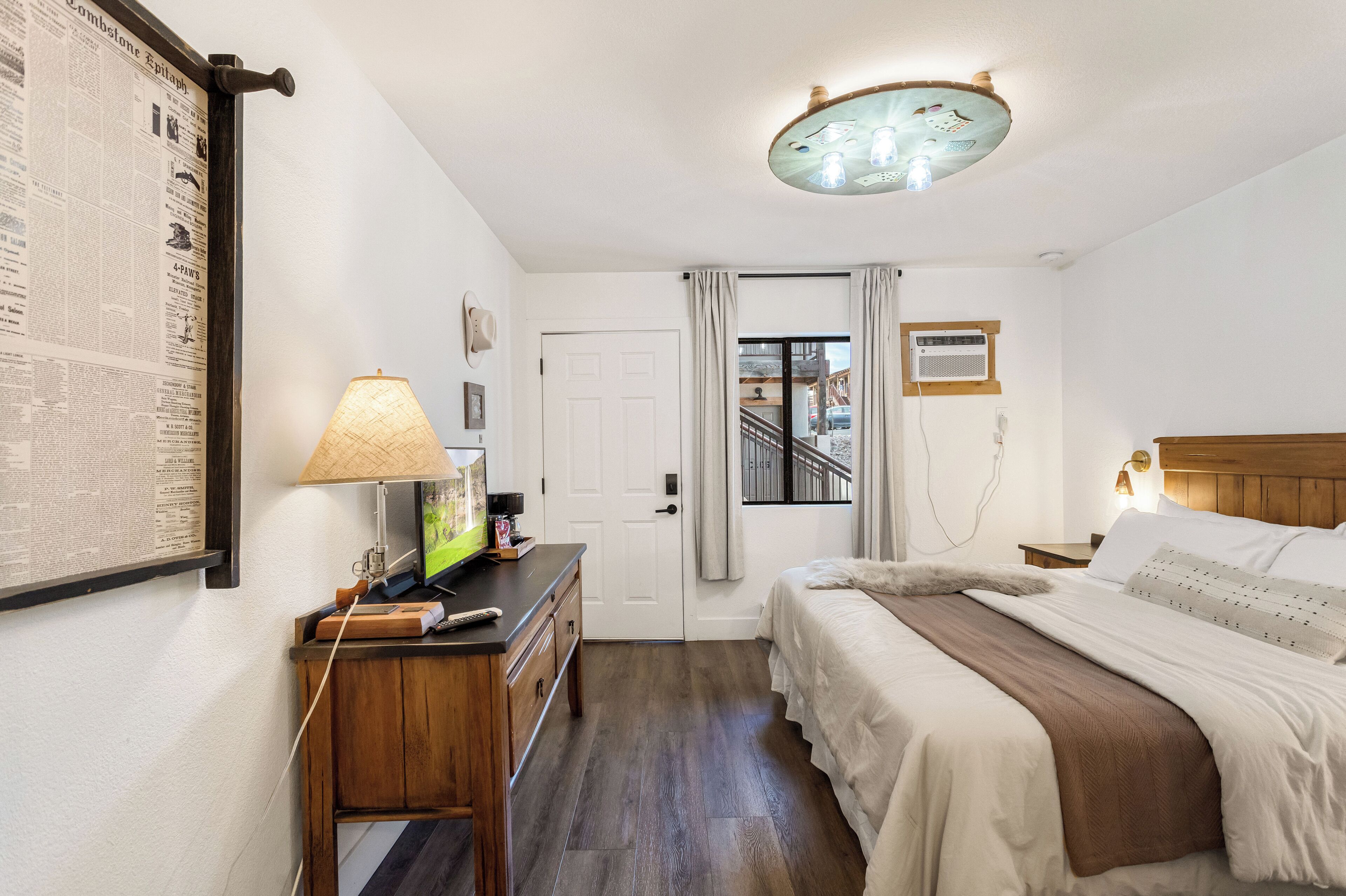 A hotel room with a bed, a desk with a lamp, a television, and a window with curtains.