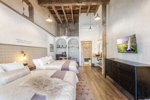 A bedroom with two beds, a wooden ceiling, a TV, and a painting on the wall.