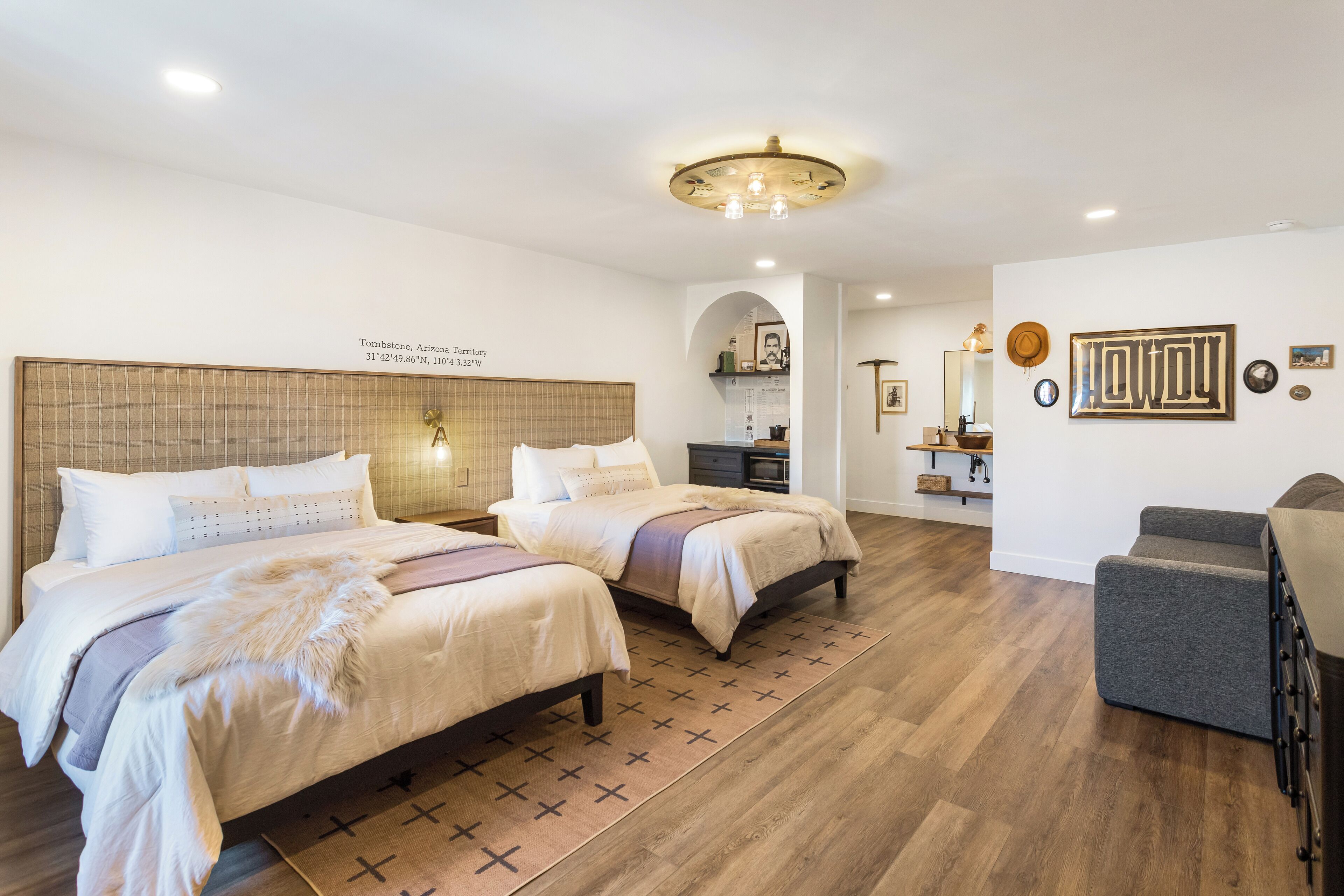 A hotel room with two beds, a sofa, a wooden floor, and a ceiling light fixture.
