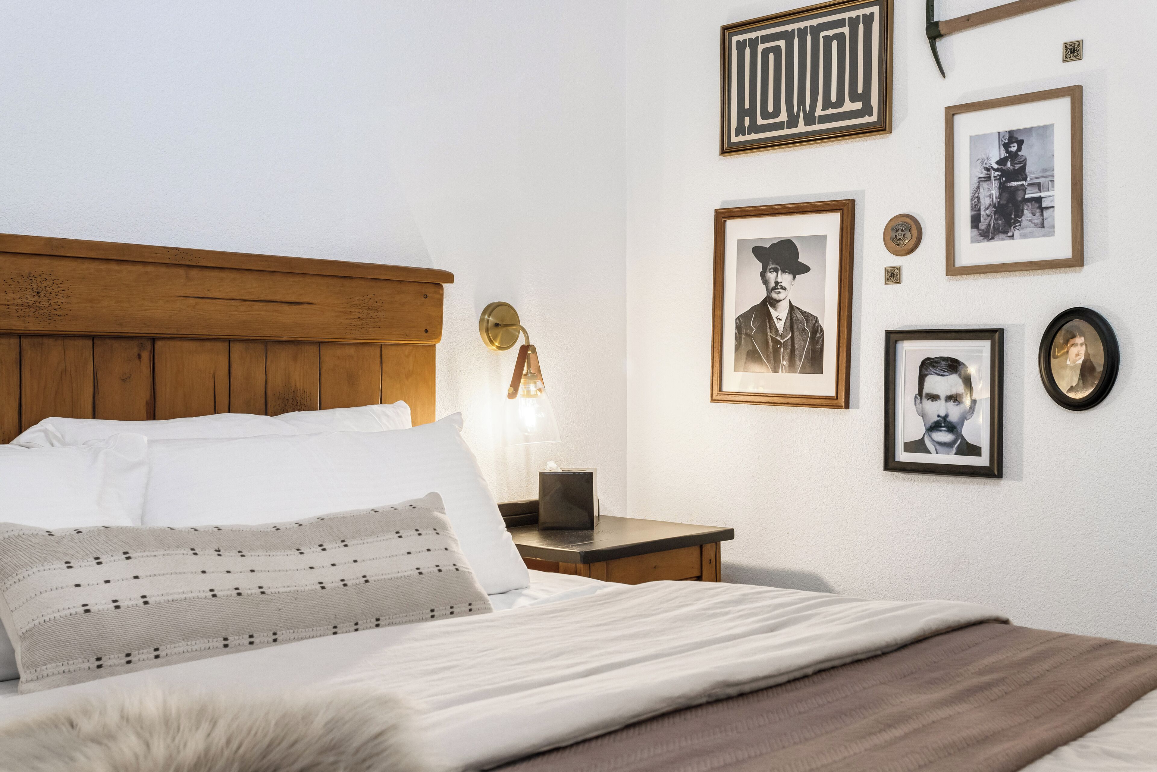 Un lit bien fait, avec une tête de lit en bois, une table de chevet avec une lampe et des tableaux encadrés accrochés au mur.