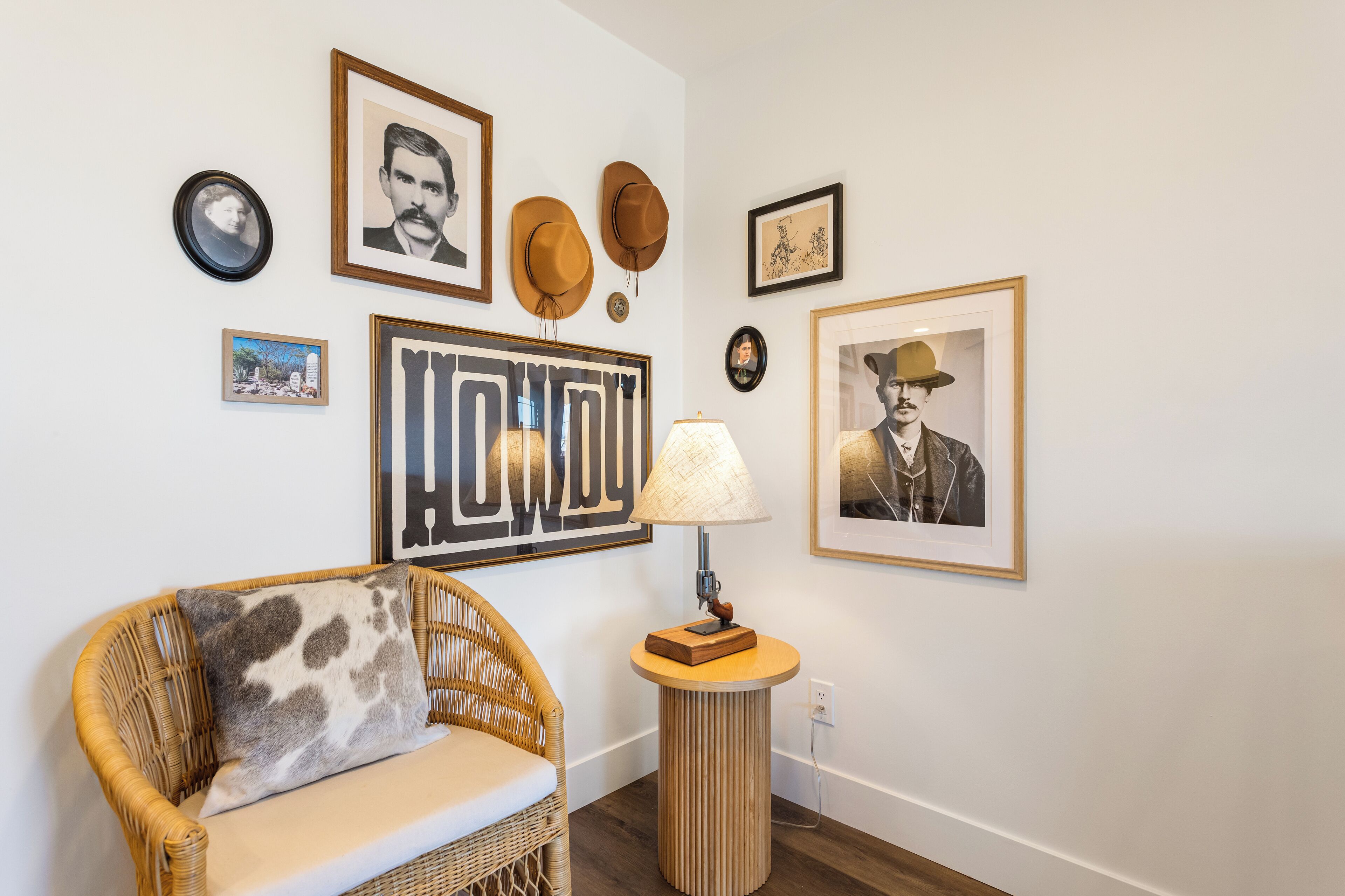 A room with a wicker sofa, a round table with a lamp, and various framed pictures on the wall.