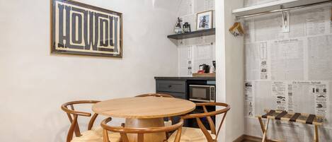 Un comedor con una mesa de madera redonda y cuatro sillas, una obra de arte enmarcada sobre la mesa, y una pared cubierta con periódicos.