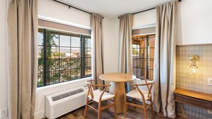 A room with a round wooden table and four chairs, a radiator, and large windows with curtains.