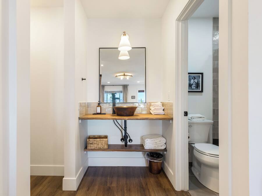 A modern bathroom with a wooden vanity, a large mirror, and a hanging light fixture.