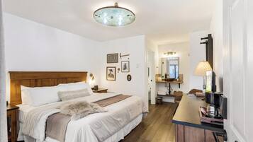 Un dormitorio con cabecera de madera, una cama grande con sábanas blancas, un plaid de piel y una mesita de noche con lámpara.