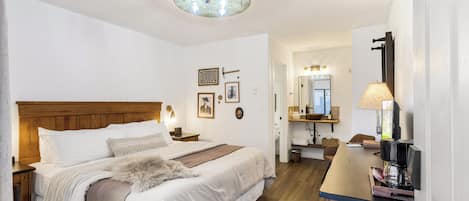 A bedroom with a wooden headboard, a large bed with white linens, a fur throw, a bedside table with a lamp, and a nightstand.