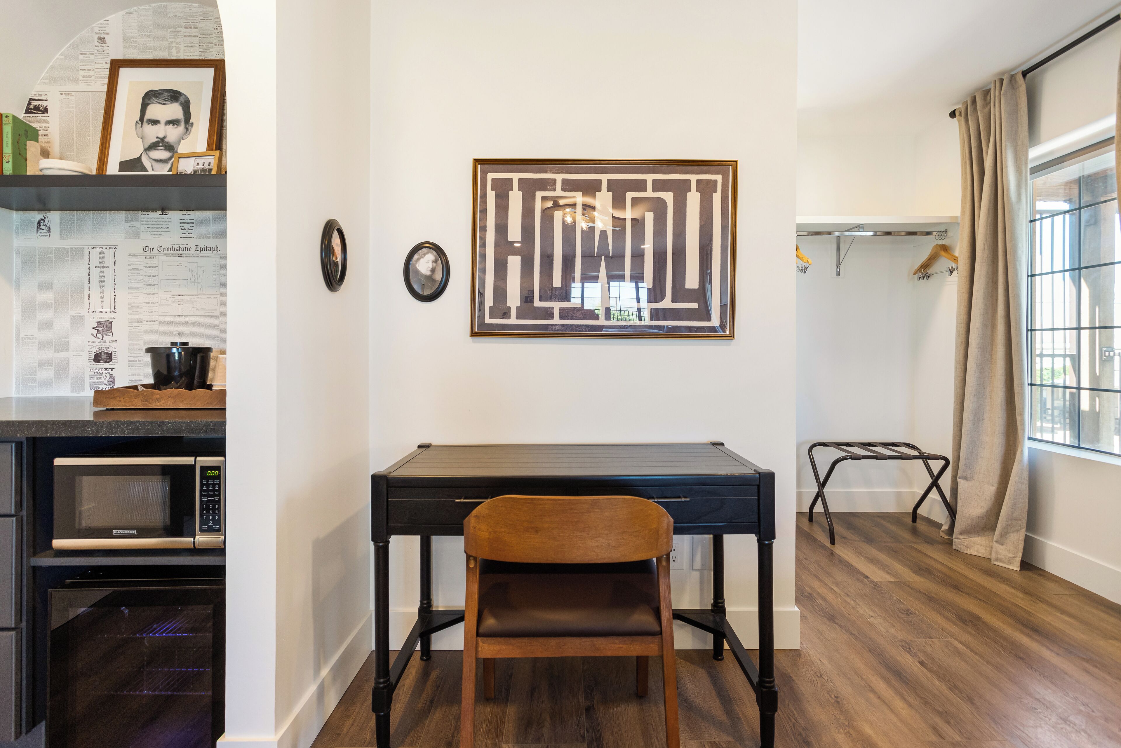 A kitchen with a microwave, oven, and a wooden chair in front of a black desk.