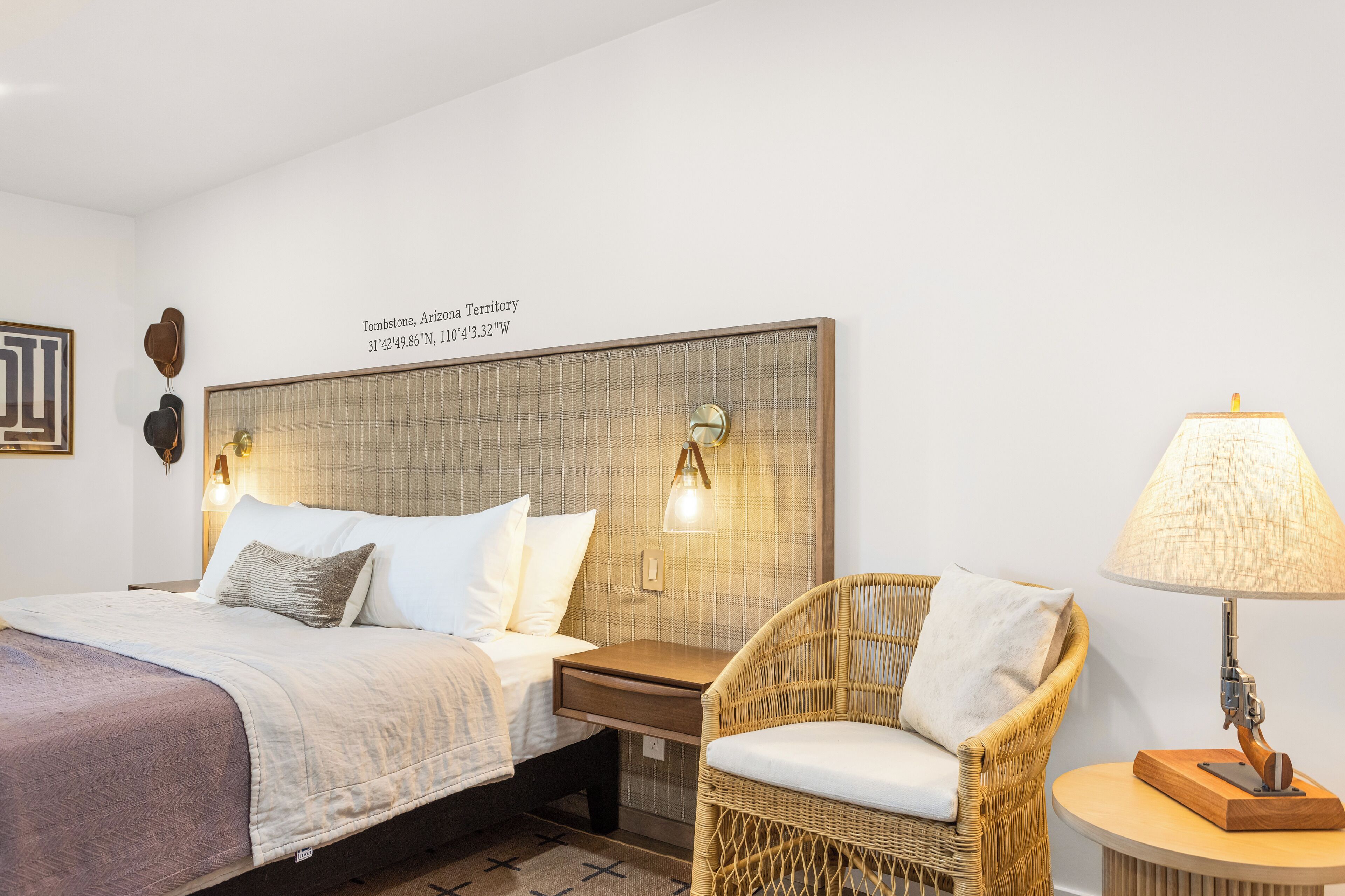 Un dormitorio con cama, mesita de noche, silla de mimbre y lámpara.