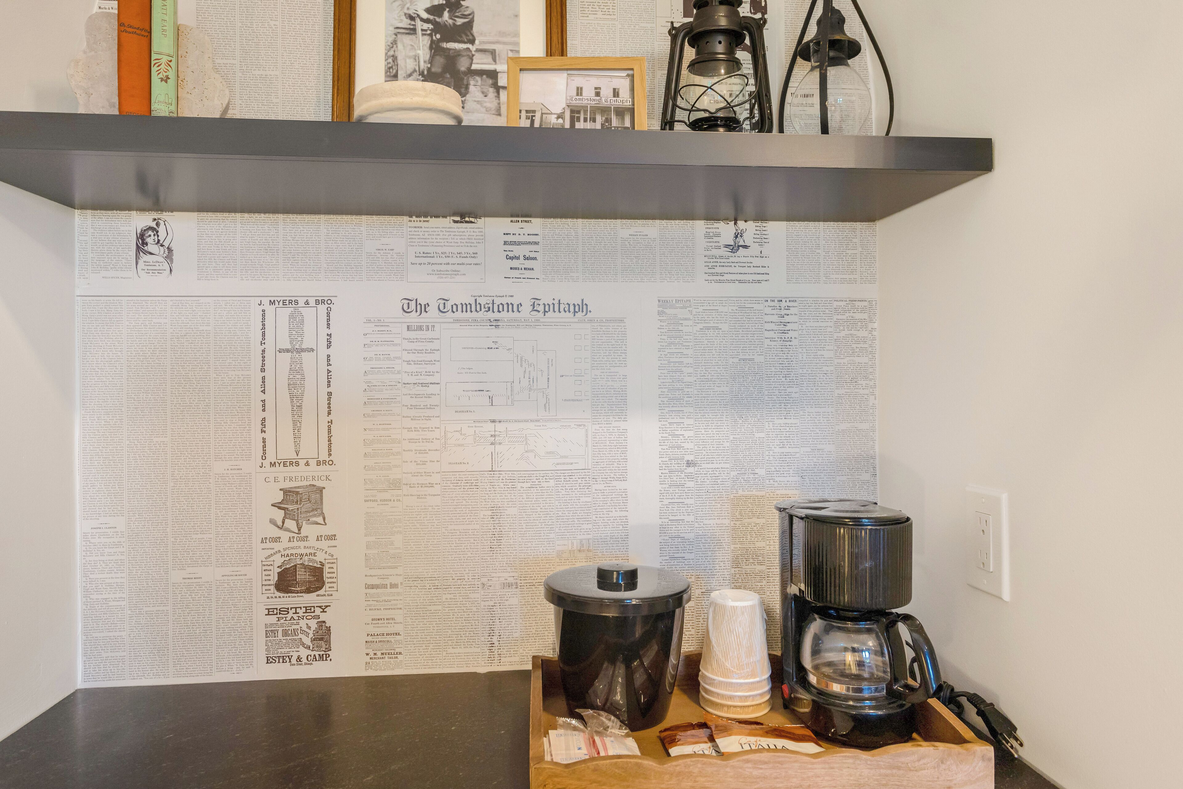 A kitchen with a coffee maker, a kettle, and a wooden cutting board.