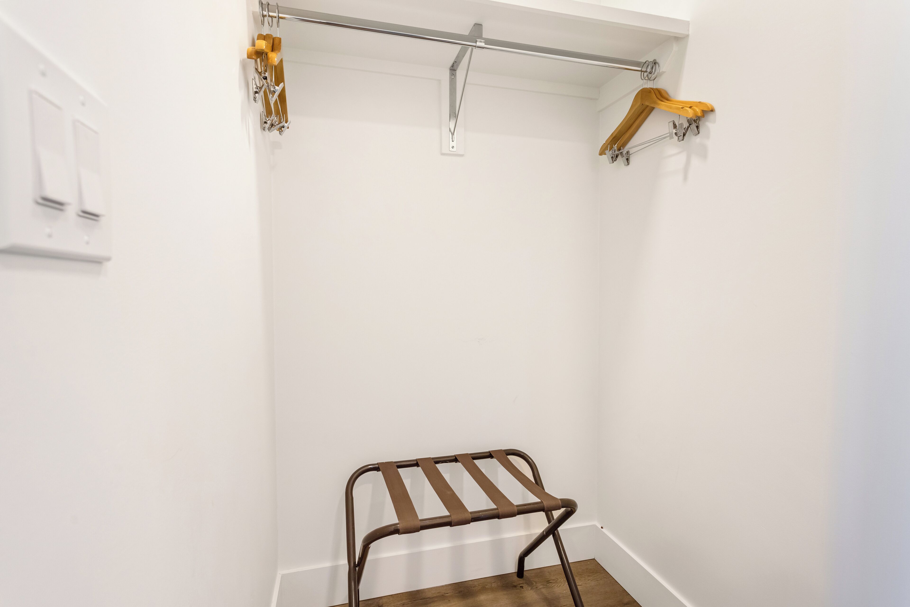 Ein kleiner, abgeschlossener Raum mit einem Metallklappstuhl, einem hölzernen Wäscheständer und einer weißen Wand mit Lichtschalter.