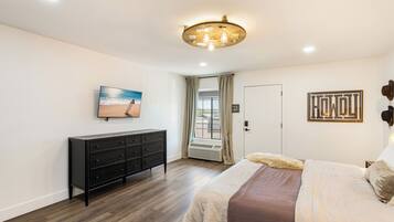 Un dormitorio con cama, cómoda, luz de techo, ventana con cortinas y una obra de arte colgada en la pared.