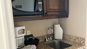 A compact kitchen with dark wooden cabinets, a stainless steel sink, a built-in microwave, and a coffee maker. - Carriage Studio Retreat (Shanty Bay)