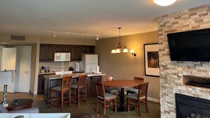 A modern kitchen with dark cabinets, a central island, and a dining area with a wooden table and chairs.